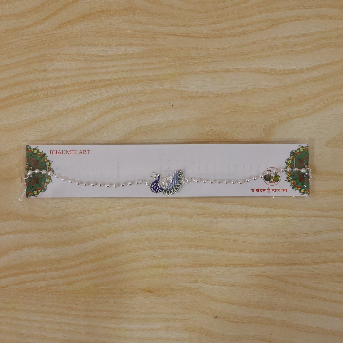 Silver peacock Rakhi styled on a festive surface for Raksha Bandhan