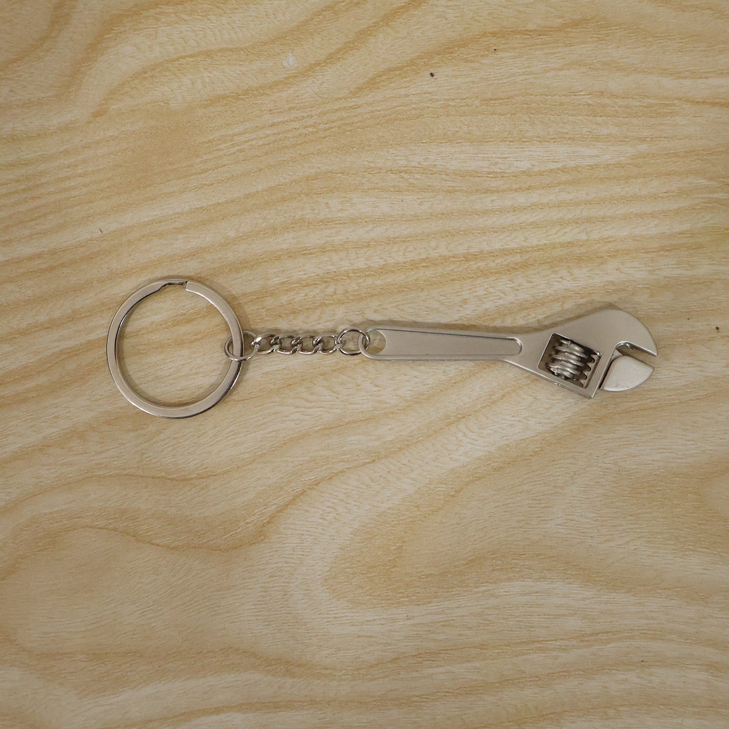 A silver metal mini adjustable wrench keychain with a key ring and chain is laid flat on a light-colored wooden surface.