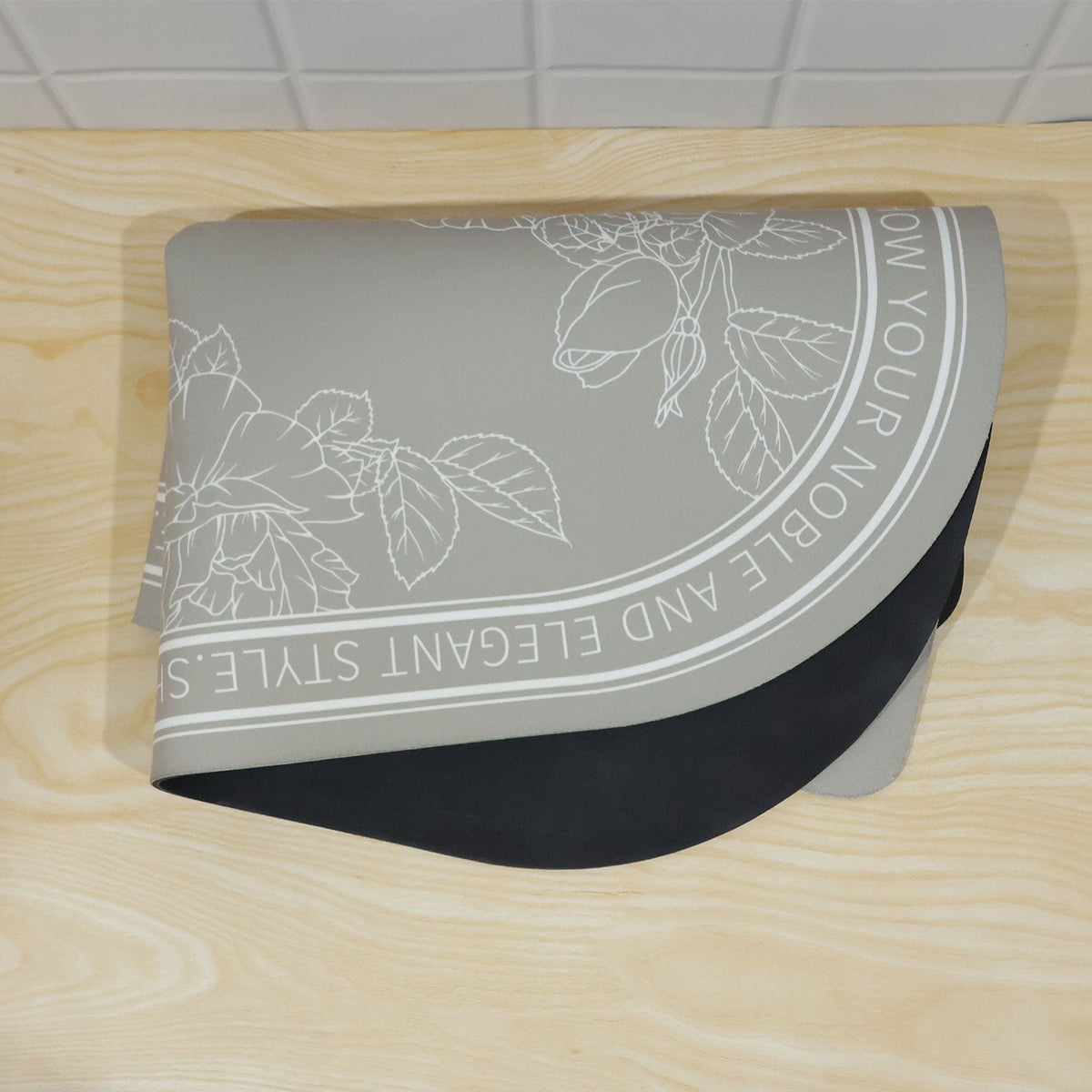 A gray half-round mat with white floral patterns and text, folded in half on a light wooden surface.