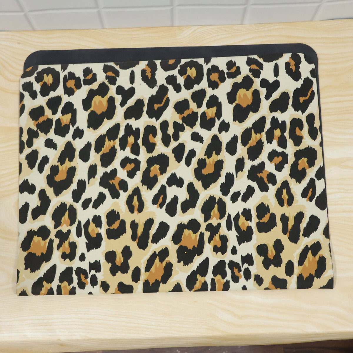 A rectangular leopard print mat with a black border, lying flat on a light wooden surface.