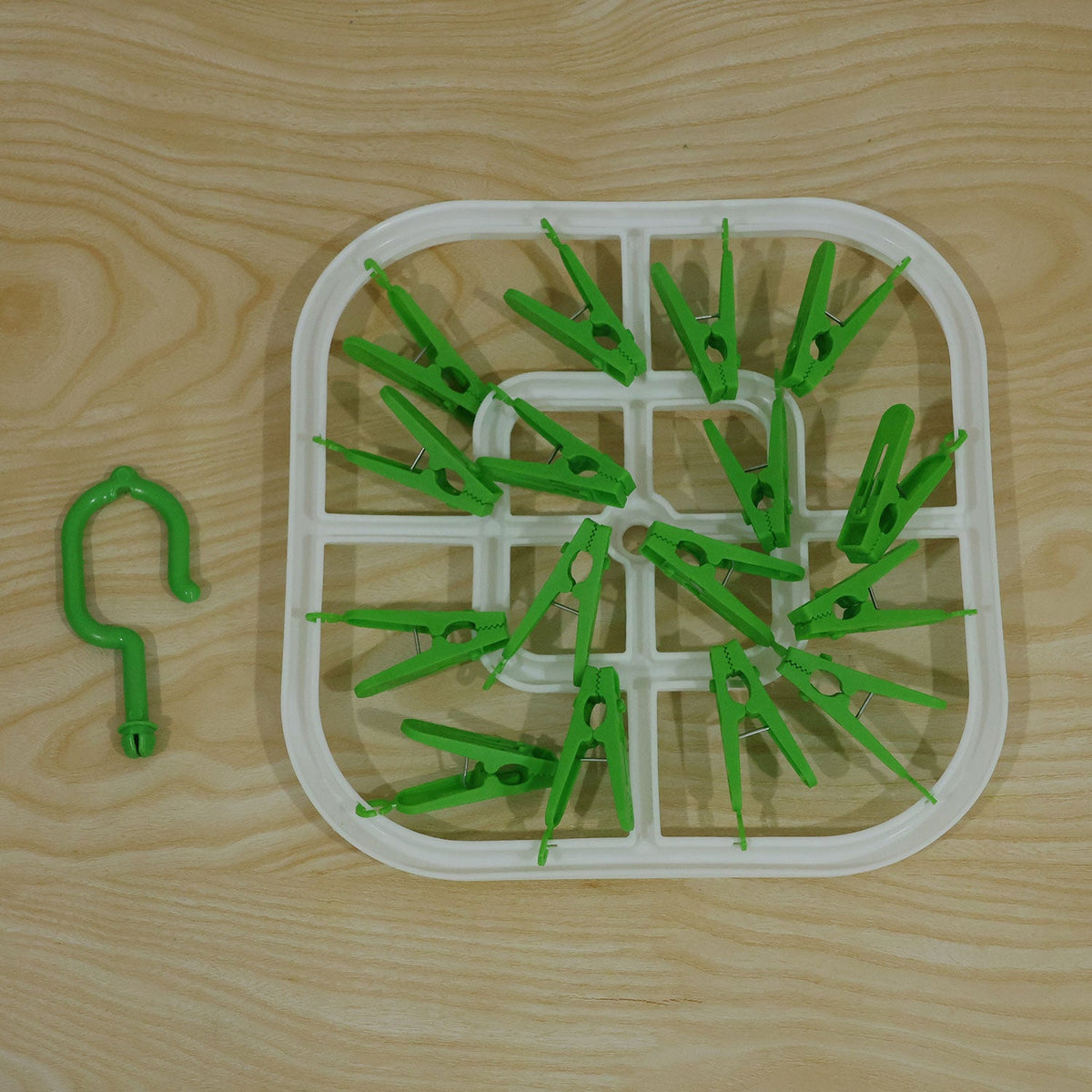 Overhead view of the white square drying rack with green clips and a detached green hook on a wooden surface.