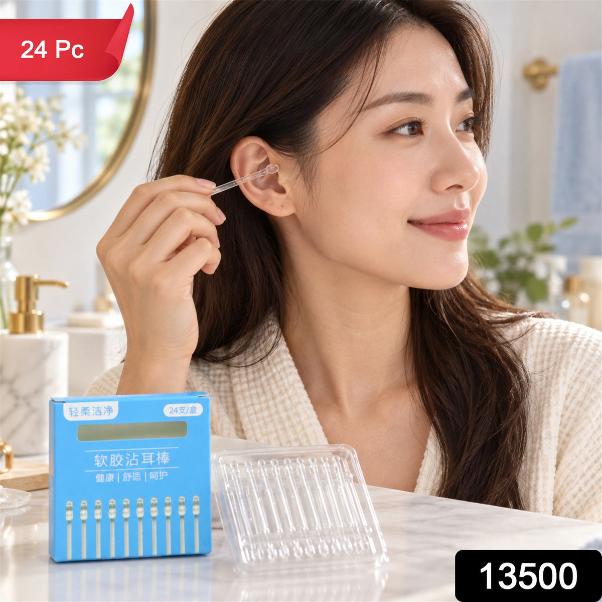 A woman uses a clear silicone ear cleaning stick in her ear, with a blue box and clear holder visible on a bathroom counter.