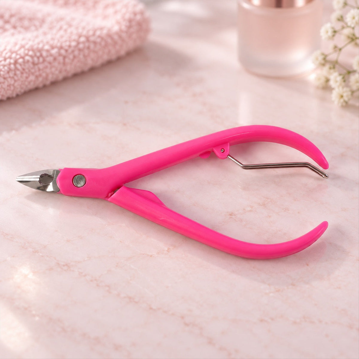 A bright pink cuticle nipper with silver-toned blades and curved handles sits on a light marble surface.