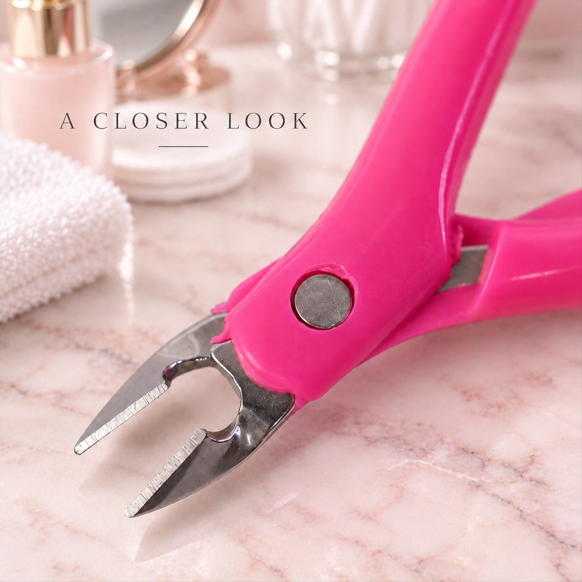 A close-up view of the metal tips and hinge of a pink cuticle nipper on a light marble counter.