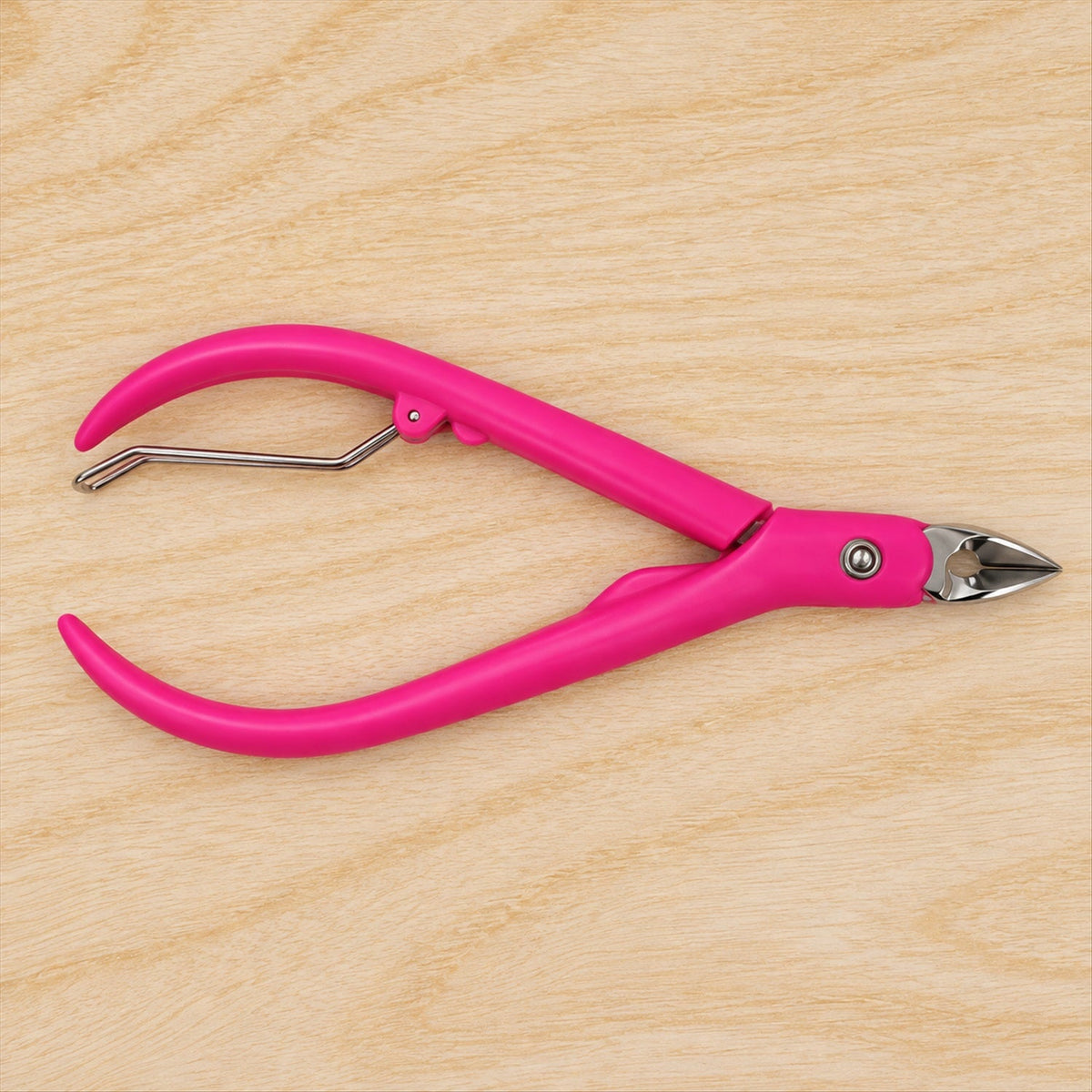A pink cuticle nipper with a silver spring and metal blades is positioned on a light wooden surface.