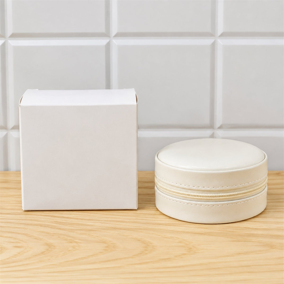 A closed cream-colored round jewellery organizer next to a plain white gift box on a light wooden surface.