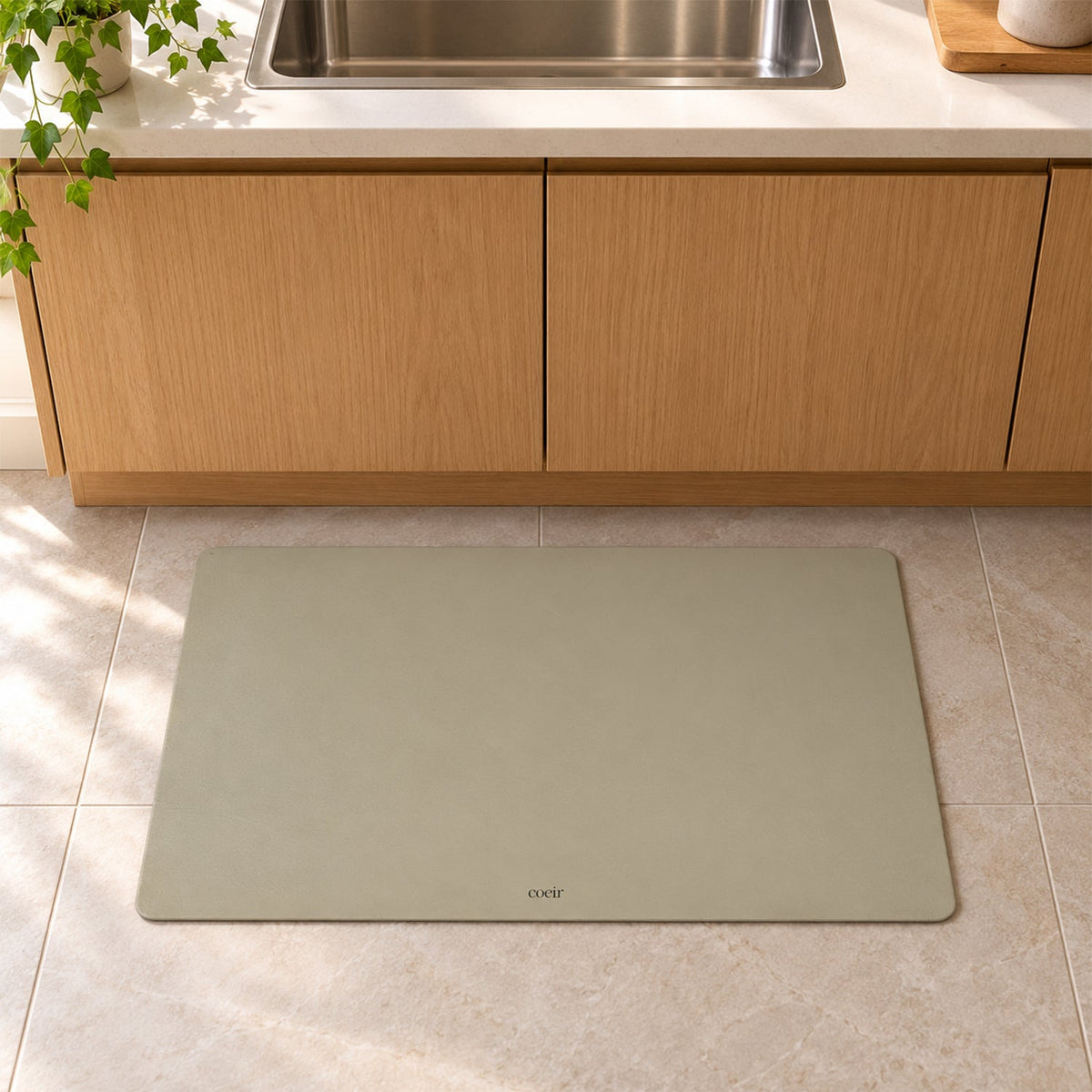 A light beige rectangular floor mat is positioned on tiled floor in front of wooden kitchen cabinets.