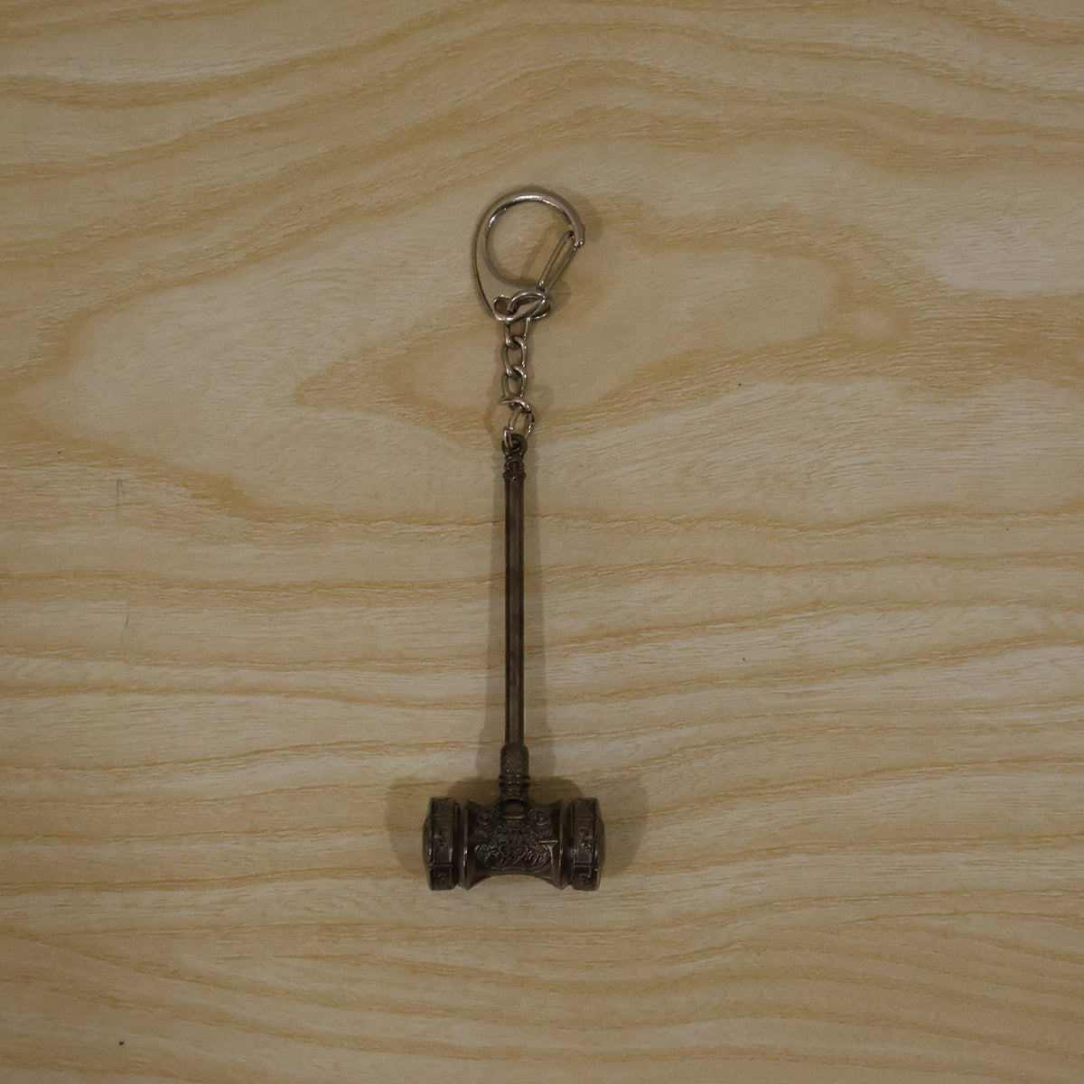 The silver-plated hammer keychain with a clip ring, displayed flat on a light-colored wooden surface.