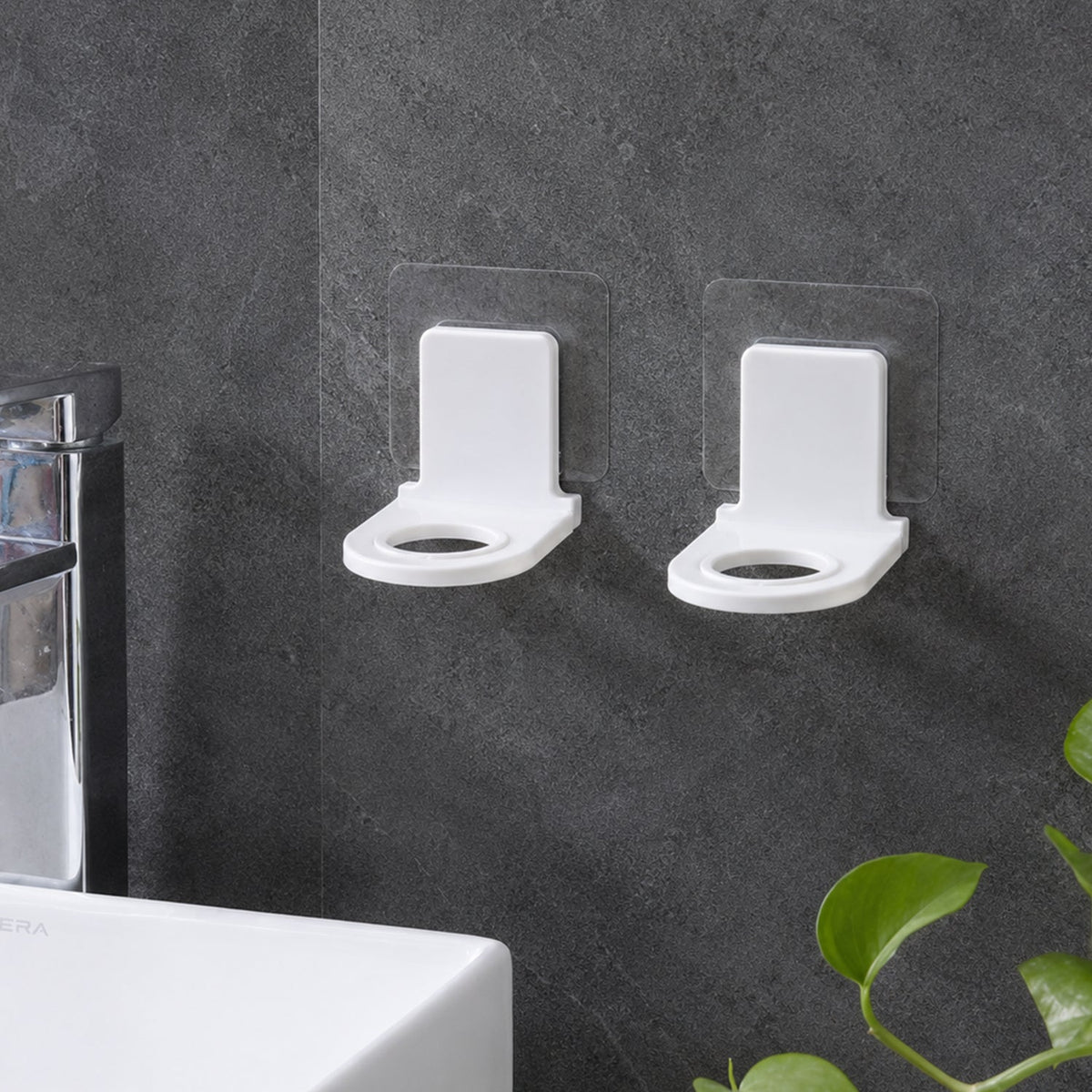 Two white plastic bottle holders with clear adhesive pads lying on a light gray tiled floor beside a white bathtub.