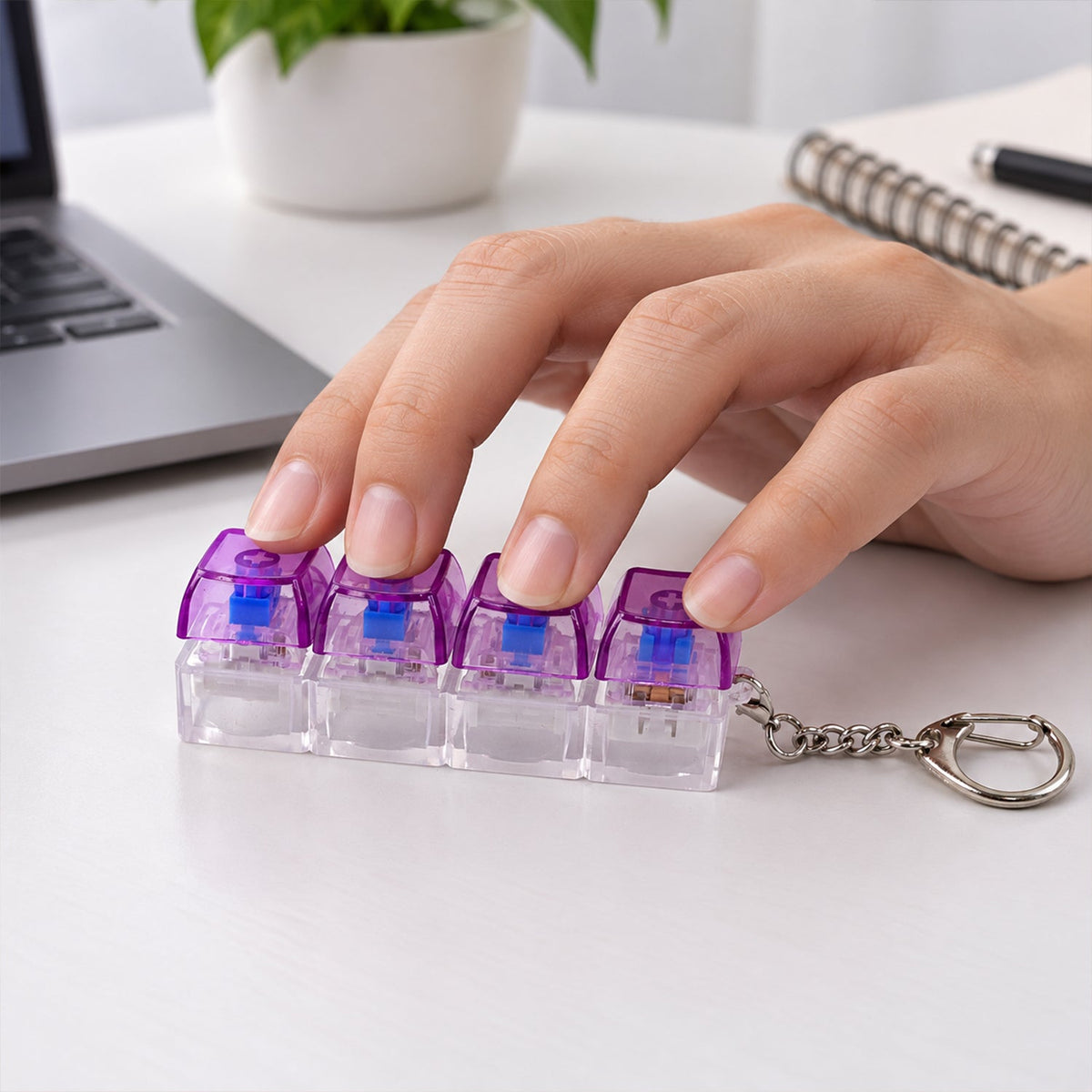 A hand presses down on the four purple and clear keyboard switches of a keychain on a white desk.