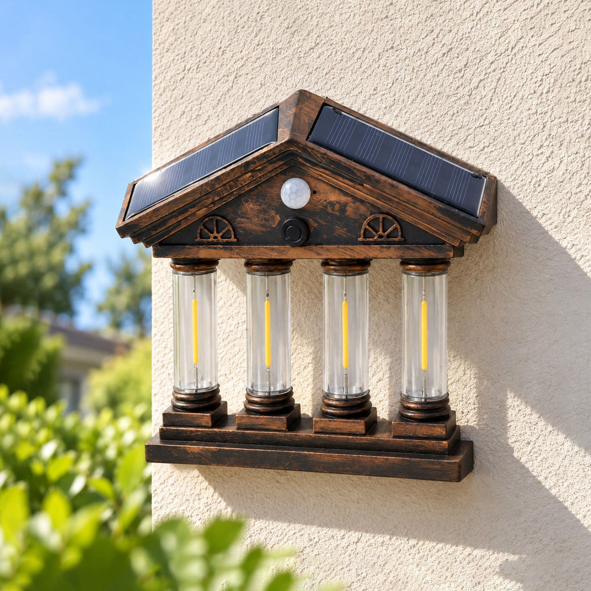 An antique bronze-colored solar wall light with four clear columns, resembling a miniature building, mounted on a