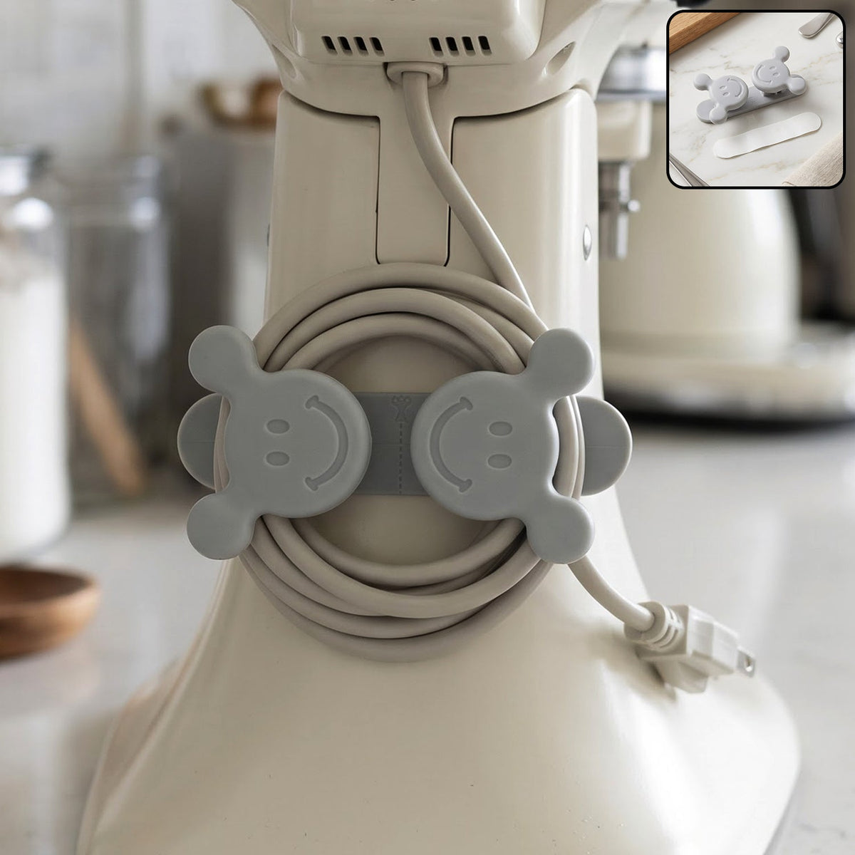 A gray silicone cord organizer with two smiling faces, holding a coiled light gray appliance cord on a white stand â€“ view 3