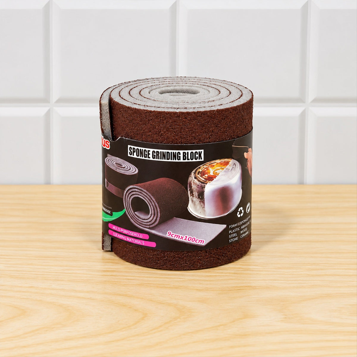 A rolled-up brown abrasive sponge with a label, standing on a light wooden table against white tiled wall.