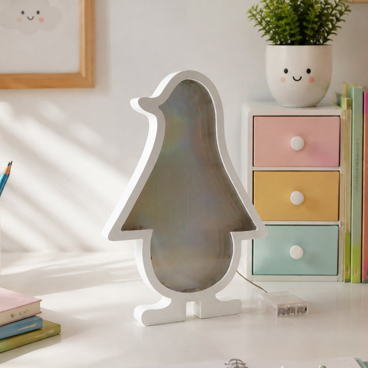 White penguin-shaped infinity mirror light unlit, on a white desk with colorful drawers and a small green plant.