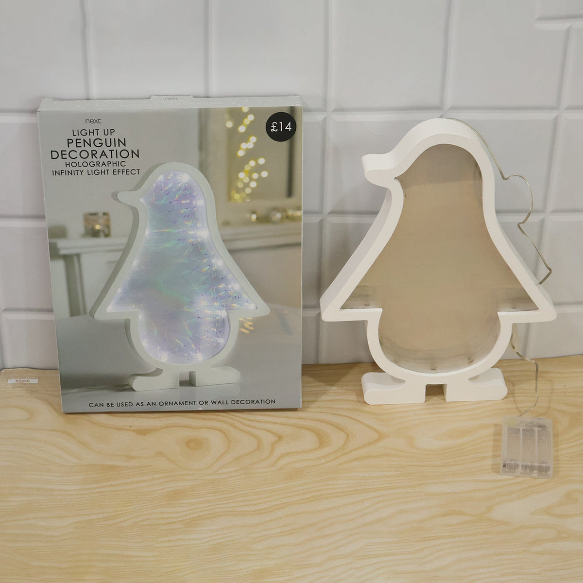 White penguin-shaped infinity mirror light unlit next to its product packaging, both on a light wooden surface.