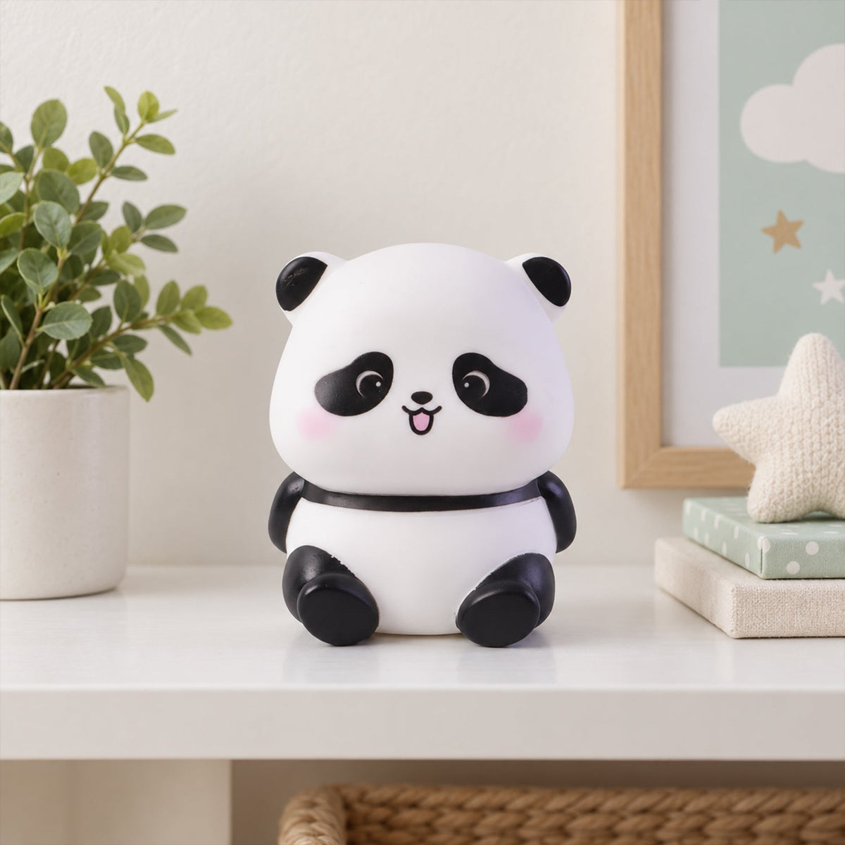 A white panda night light with black features sits on a white shelf with a potted plant, framed art, and a star pillow.