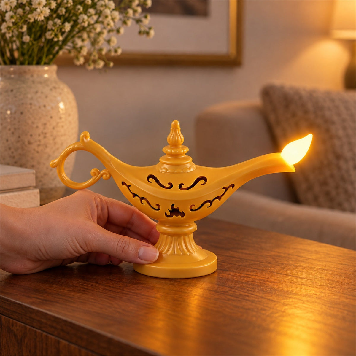 A hand holds a glowing yellow Aladdin's lamp LED light on a wooden table, with a floral vase in the background.