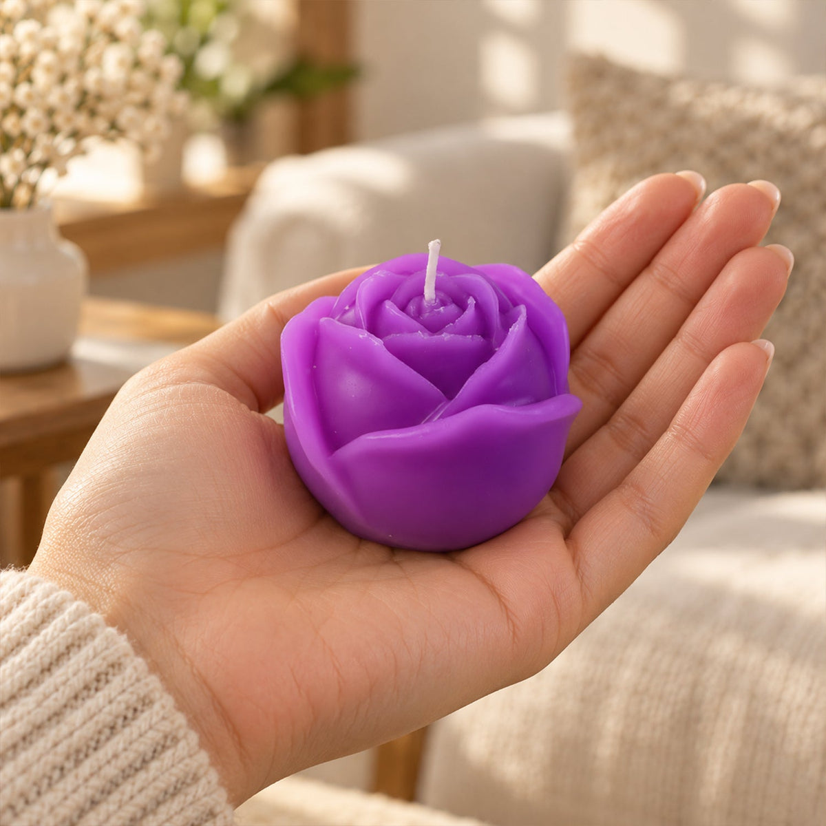 A purple rose-shaped candle rests in the palm of a hand, with a blurred living room in the background.