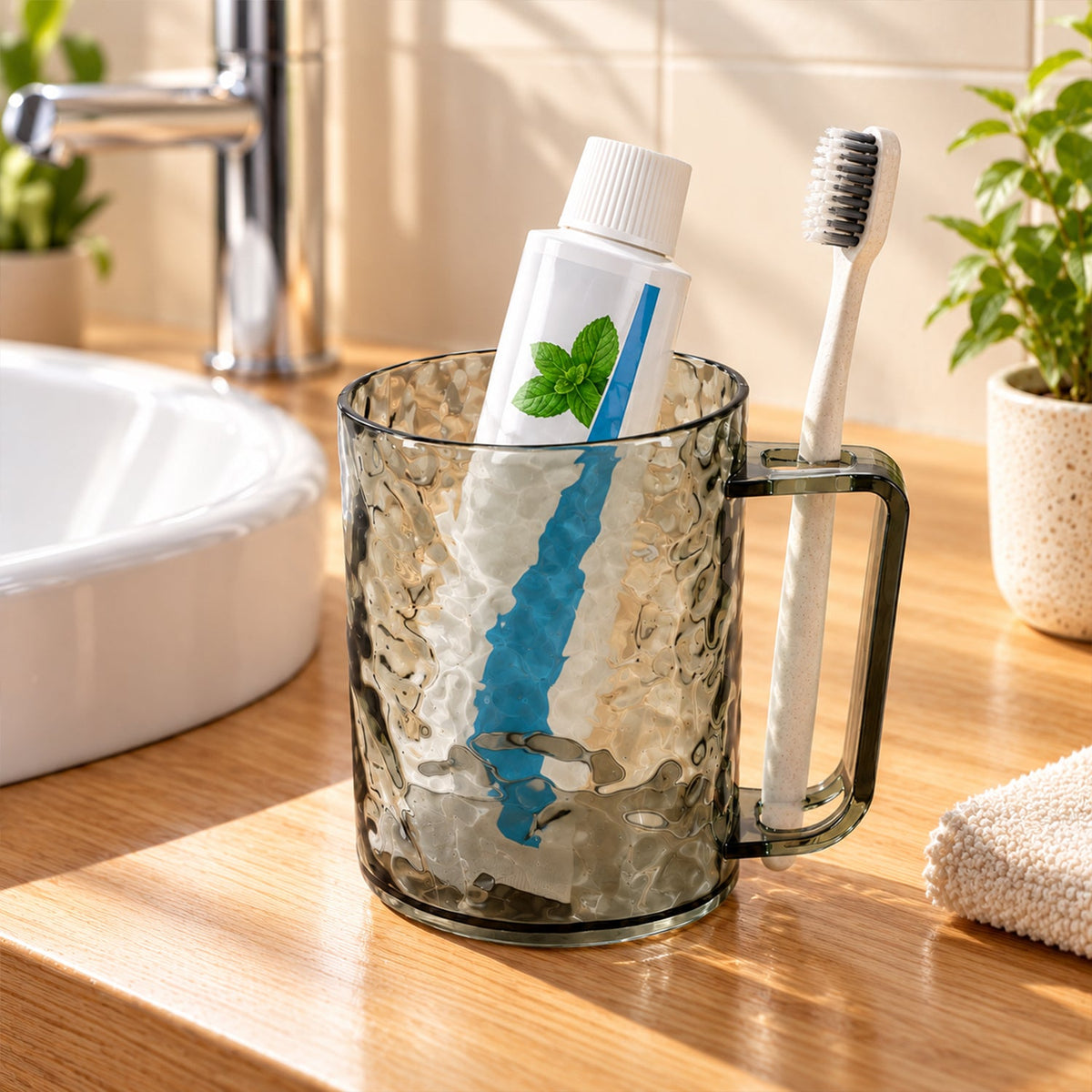 Dark grey textured plastic mug holding a white toothpaste tube and a toothbrush on a wooden bathroom counter.