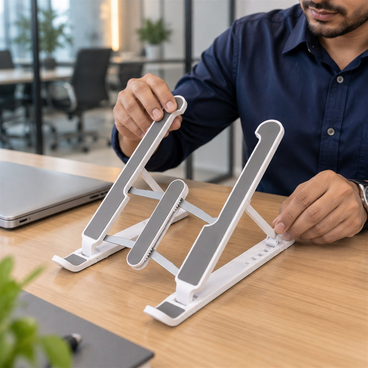 Man adjusting the height of a white and gray laptop stand on a wooden desk in an office.
