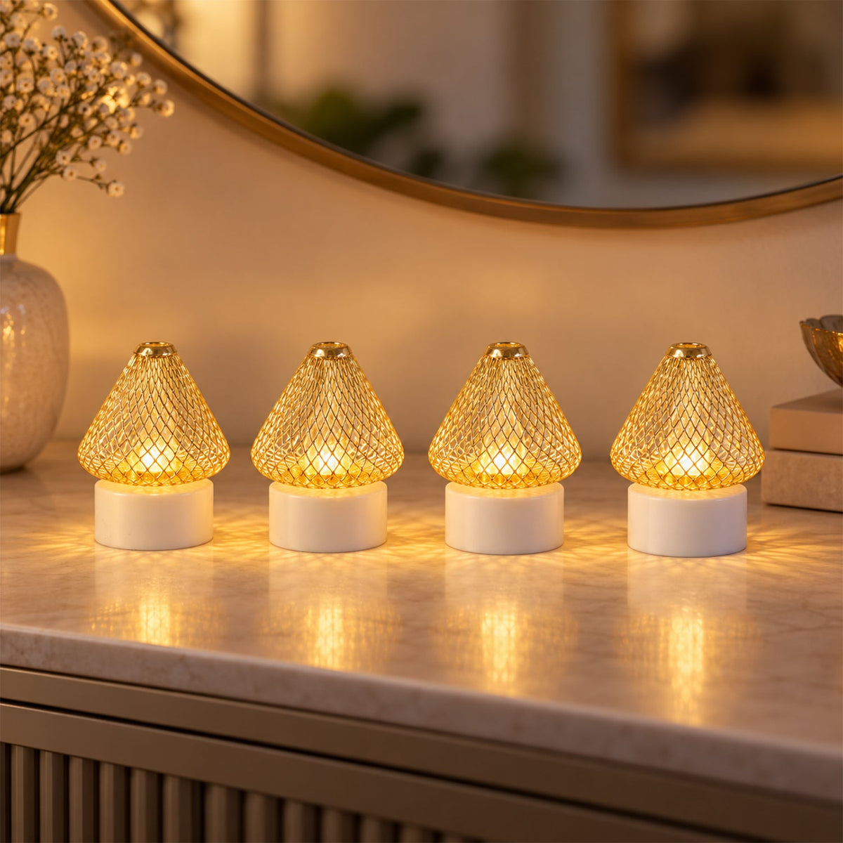 Four golden mesh LED lights with white bases cast a warm glow on a marble surface, reflecting in a round mirror.