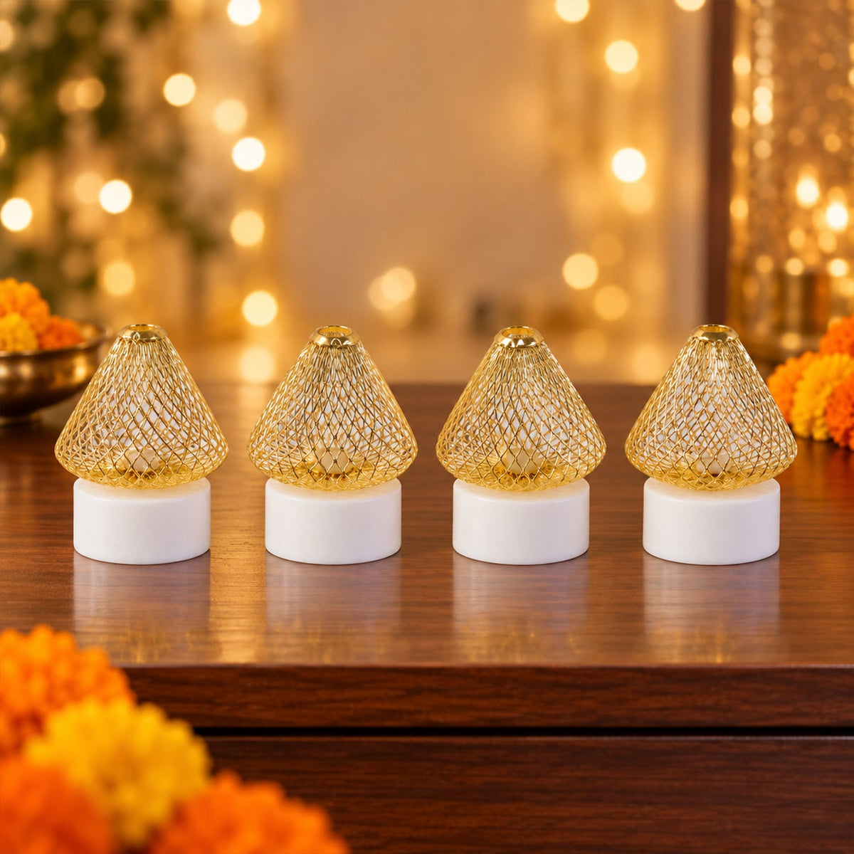 Four golden mesh LED lights with white bases on a wooden surface, surrounded by orange and yellow marigold flowers and bokeh