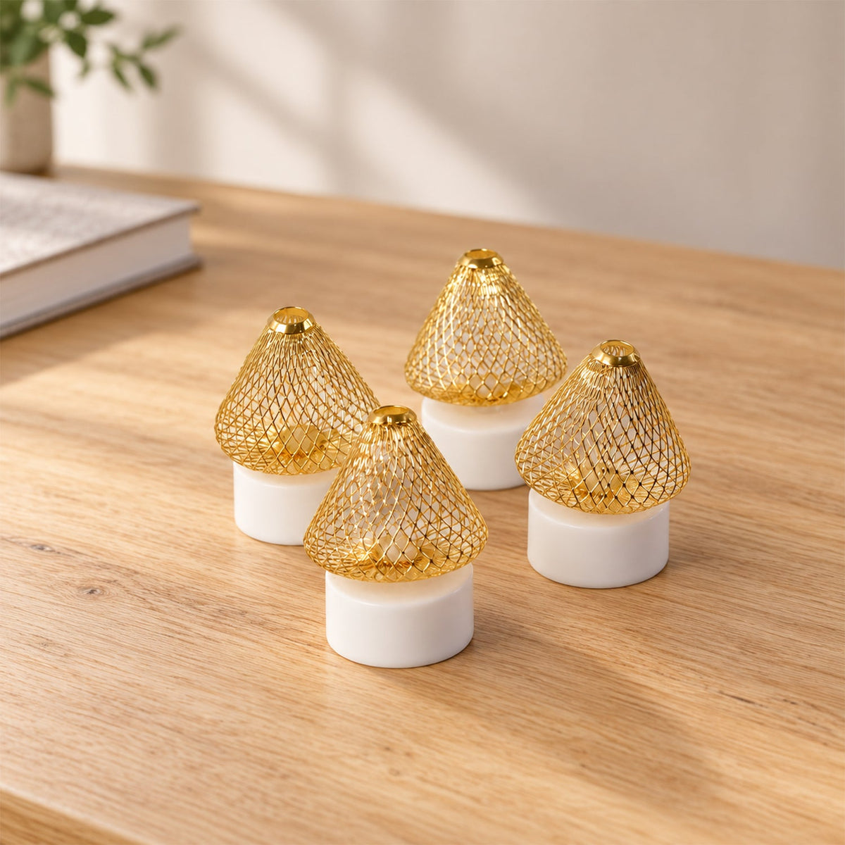 Four golden mesh LED lights with white bases are clustered together on a light wooden desk with a book and plant.