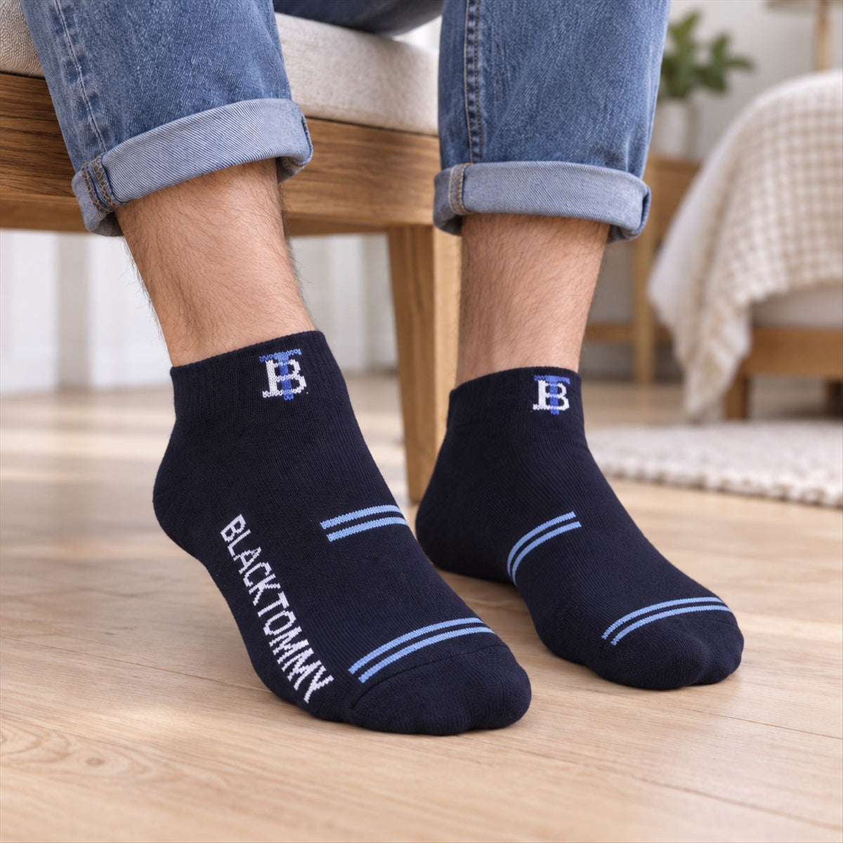 A person wears dark blue ankle socks with light blue stripes and "BLACK TOMMY" text on a wooden floor.