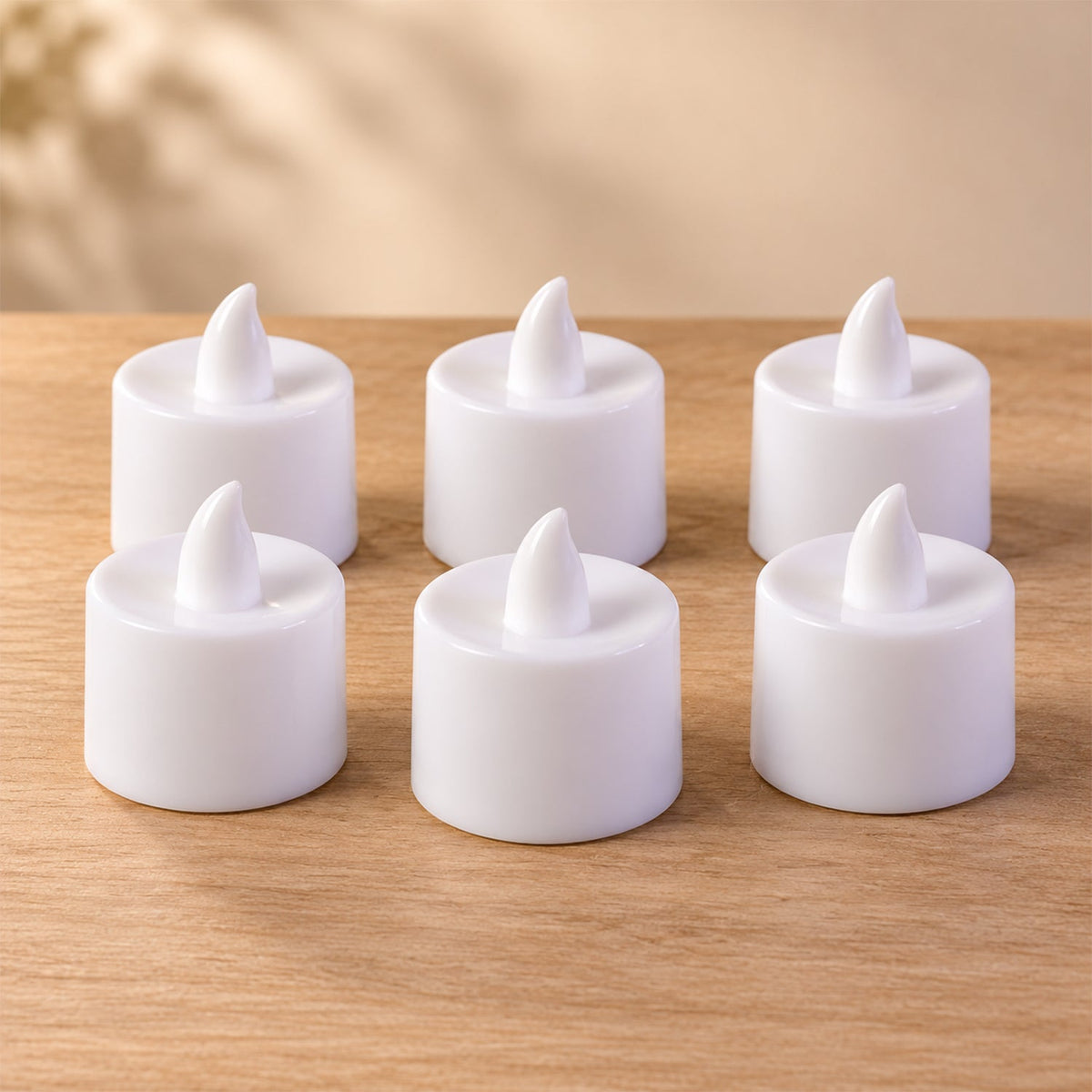 Six white flameless tealight candles are arranged in two rows on a light wooden surface, casting soft shadows.
