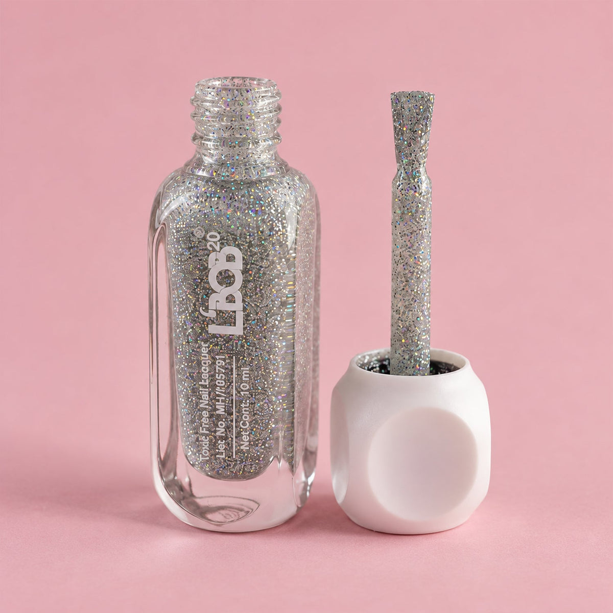 An open bottle of silver glitter nail polish sits next to its white cap with an attached brush on a pink background.