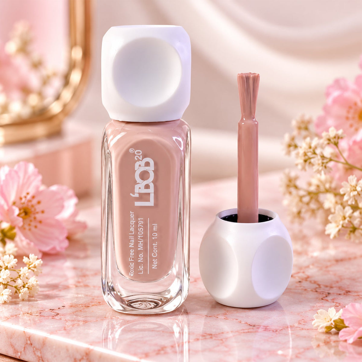 A bottle of nude pink nail polish and its brush applicator stand on a marble surface with pink flowers.