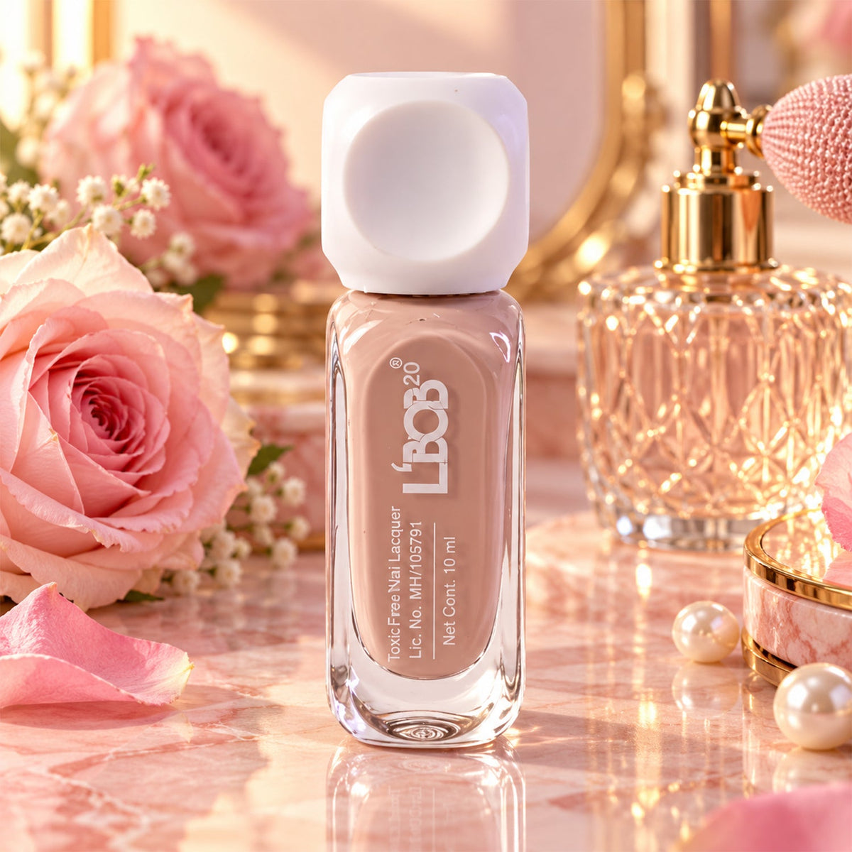 A bottle of nude pink nail polish stands on a marble surface with pink roses and perfume in the background.