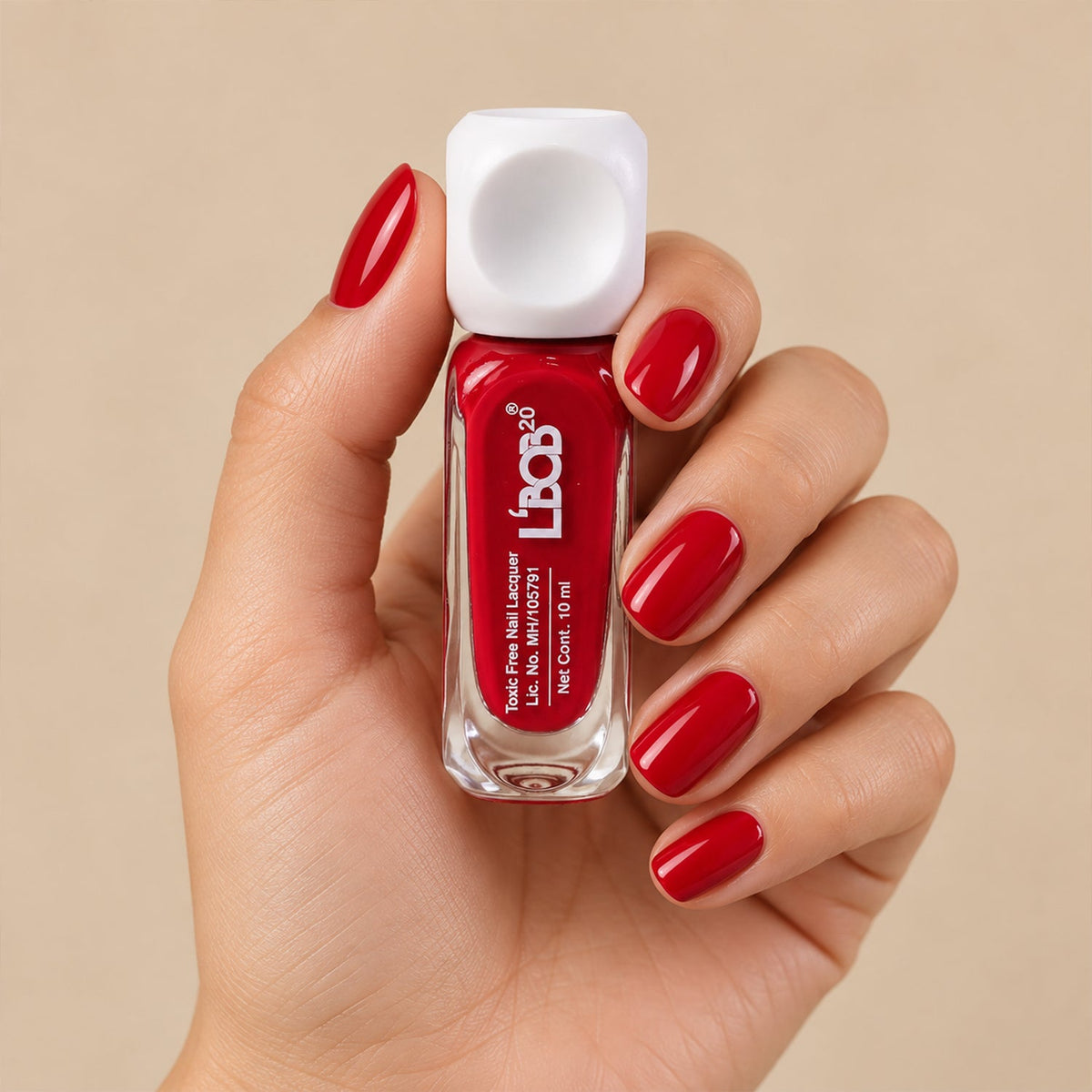 A hand holds a small clear bottle of red nail polish with a white square cap, against a light background.