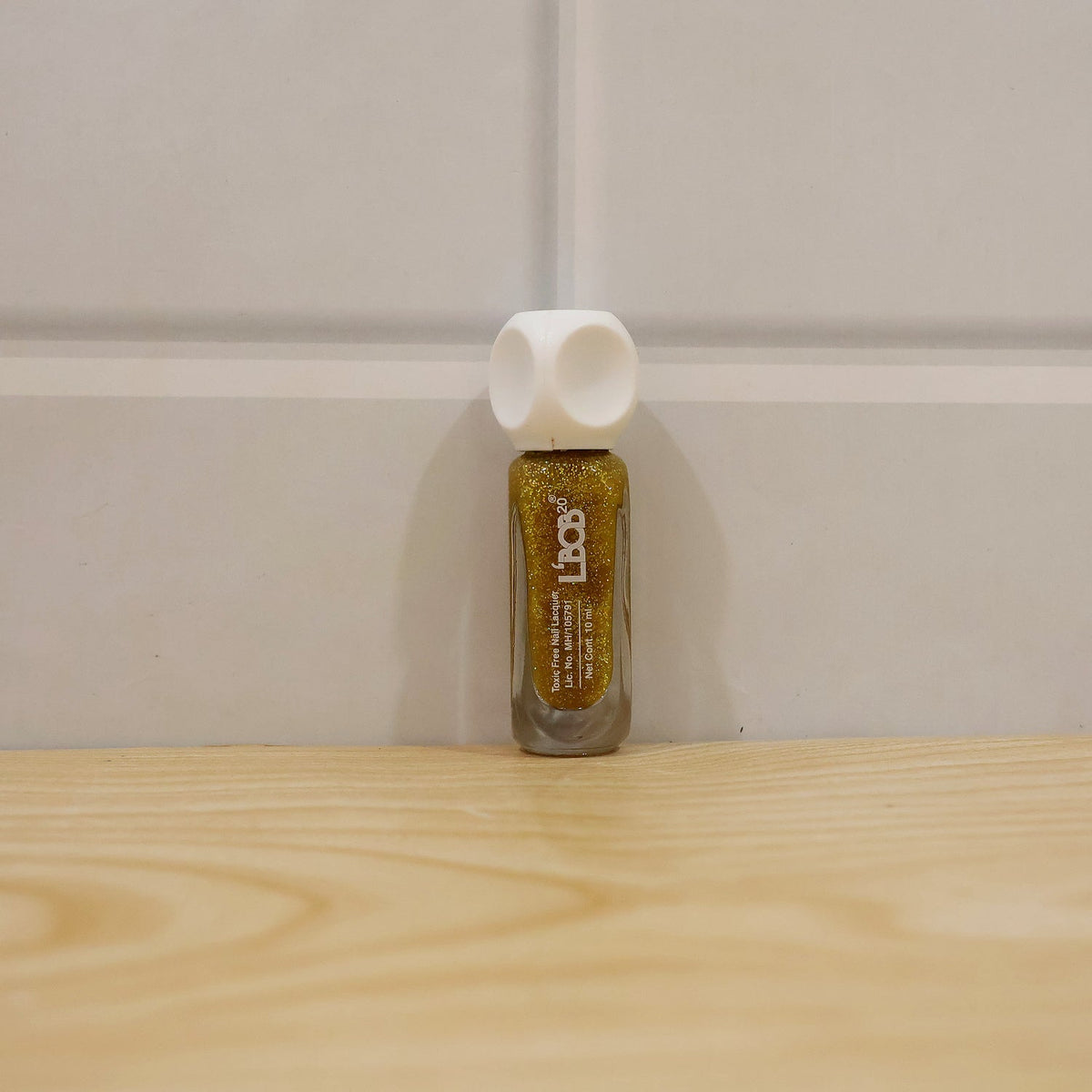 A bottle of gold glitter nail polish with a white cap sits on a wooden surface.