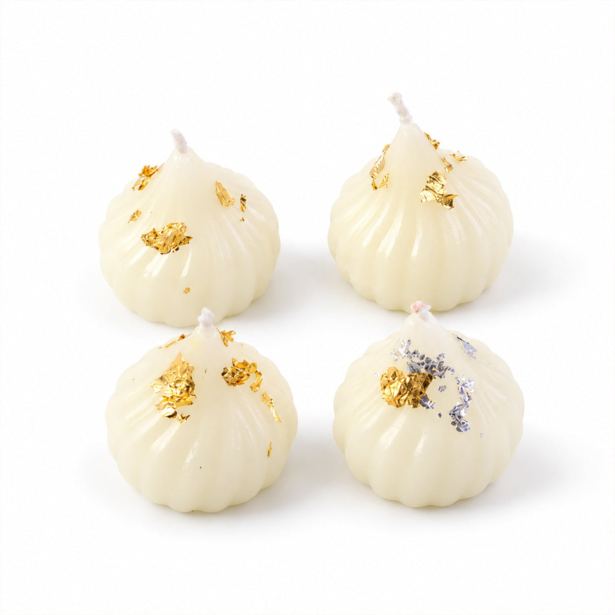 Four unlit white modak-shaped wax candles, two with gold flakes and two with silver flakes, arranged on a white background.