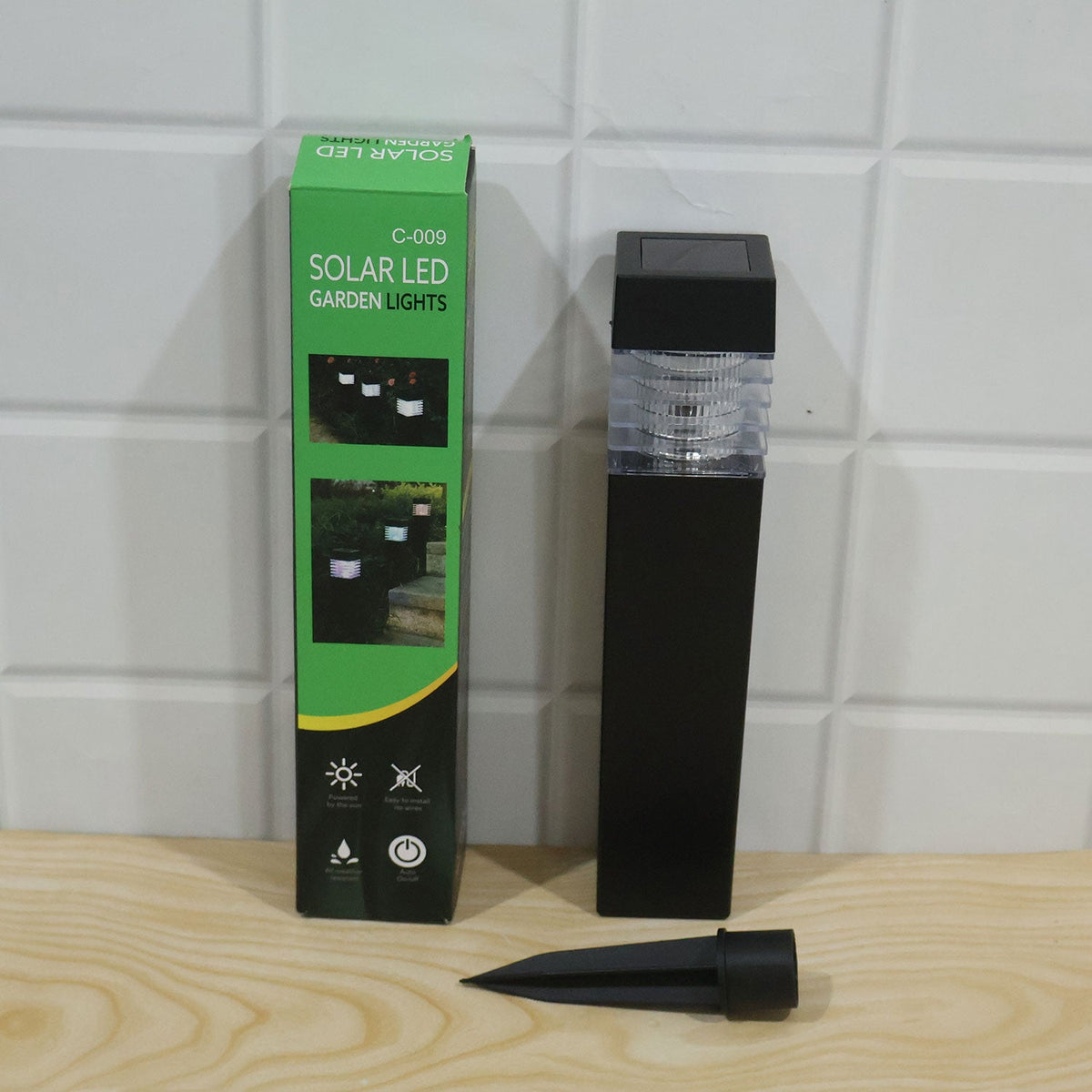 A green box labeled "Solar LED Garden Lights" next to a black solar light and its detached ground stake on a wooden surface.