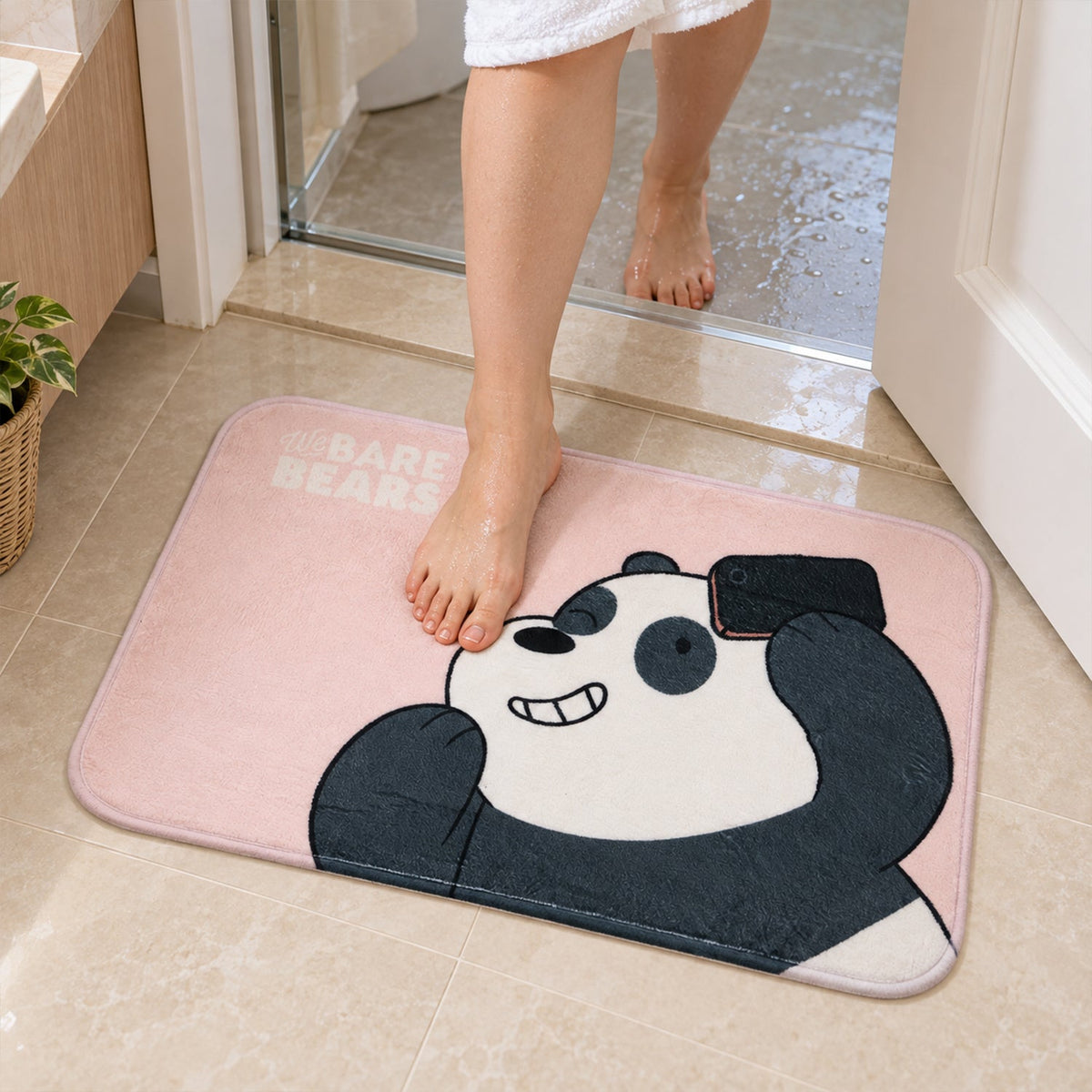 A person's bare foot steps onto a pink panda mat placed on tiled floor at a bathroom entrance.