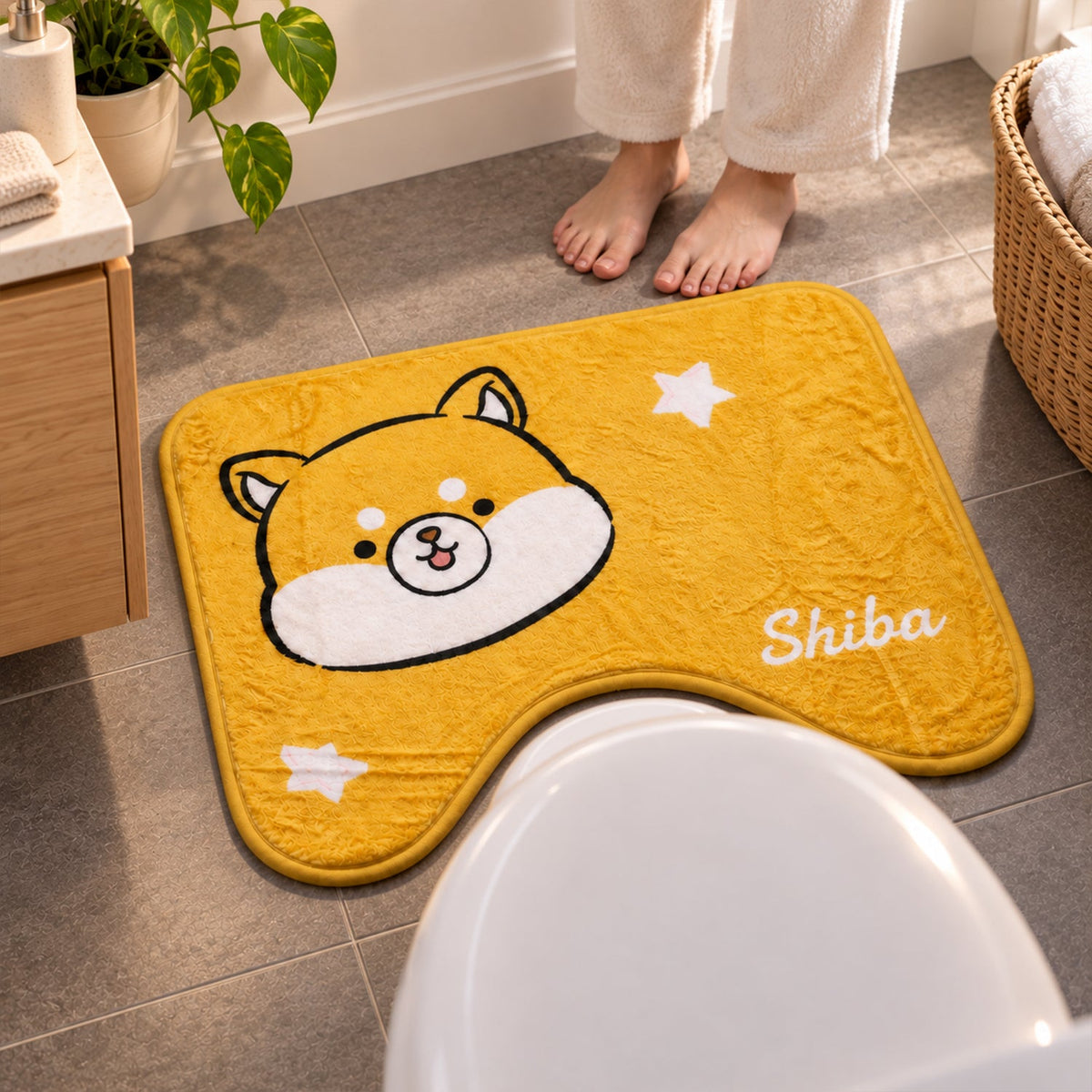 A person's bare feet stand on a grey tiled floor next to a yellow U-shaped toilet mat with a Shiba Inu character.