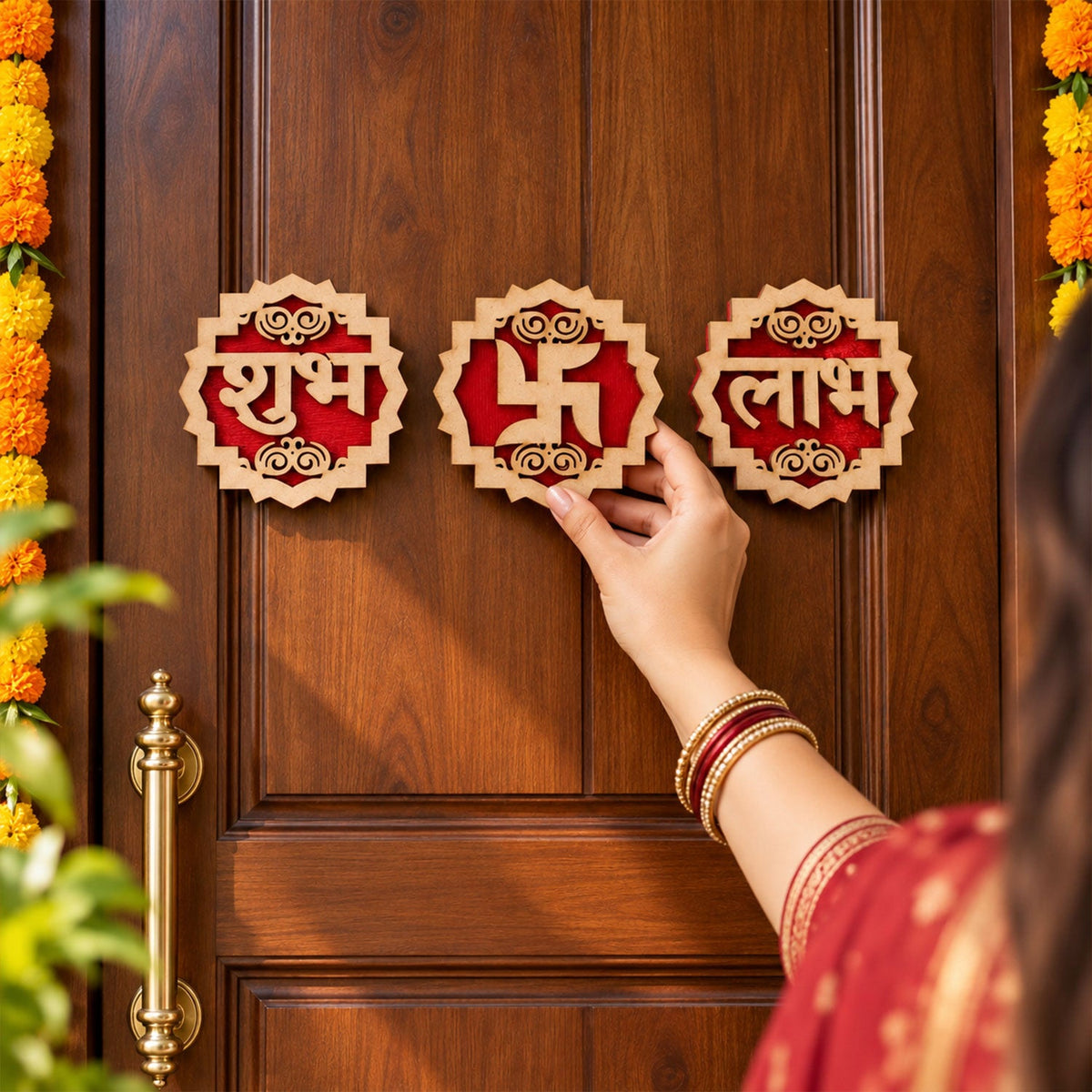 A person's hand with bangles places a wooden Swastik decoration on a dark brown door, alongside two other pieces.