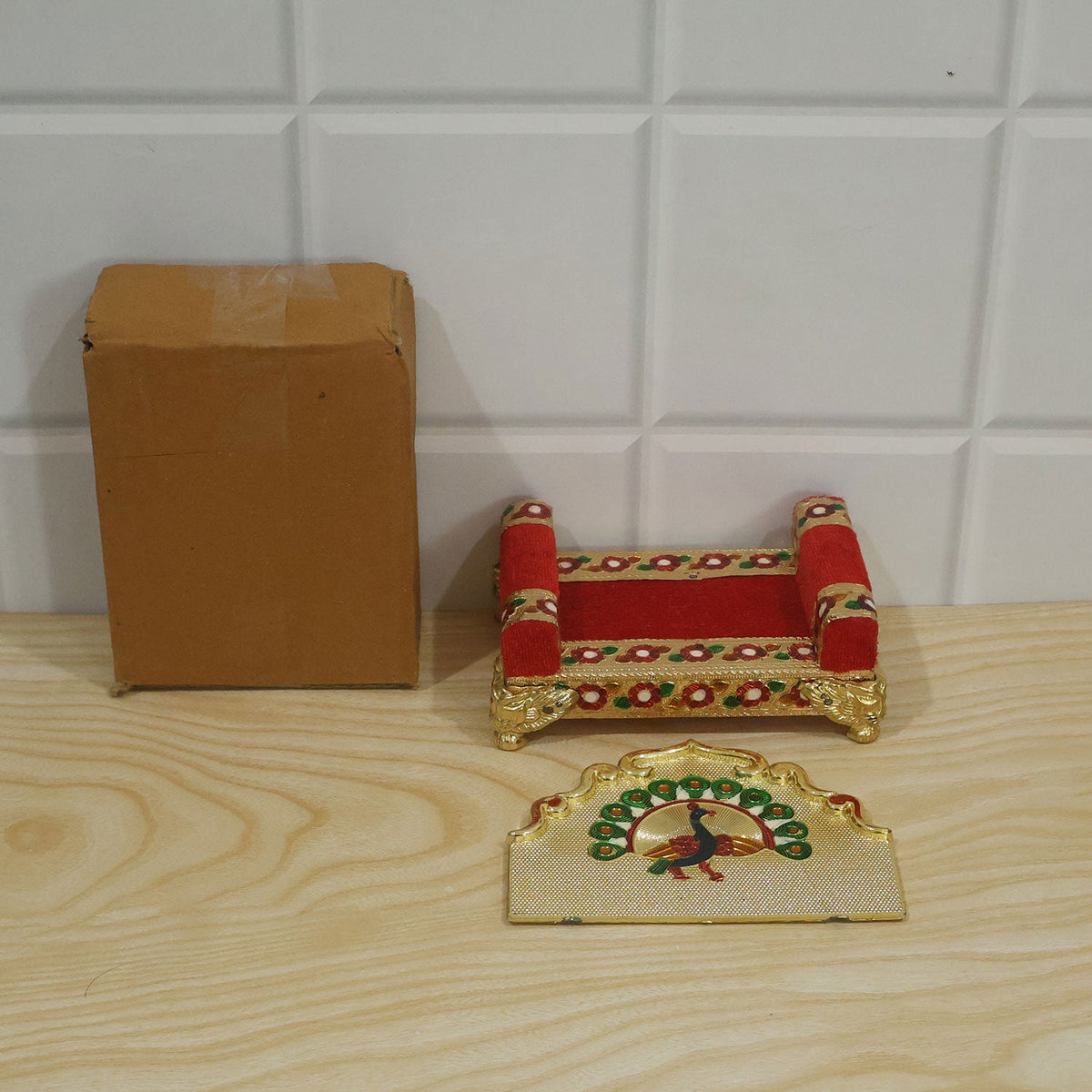 A disassembled gold and red throne with a peacock design, next to a brown cardboard box on a wooden surface.
