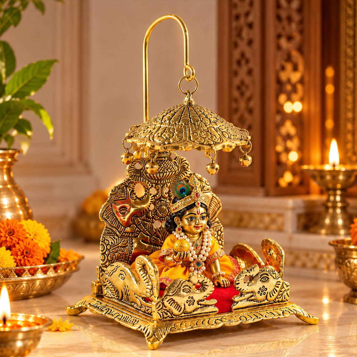 A gold-colored brass deity throne with a red velvet seat and a small idol of Krishna, surrounded by flowers and a lamp.