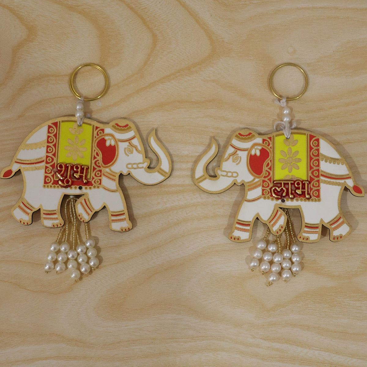 A pair of white and yellow elephant hangings with red accents and pearl tassels lie on a light wood surface.