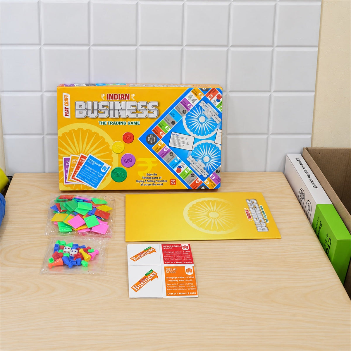 The Indian Business game box, folded board, and various game pieces are neatly arranged on a light wooden surface.