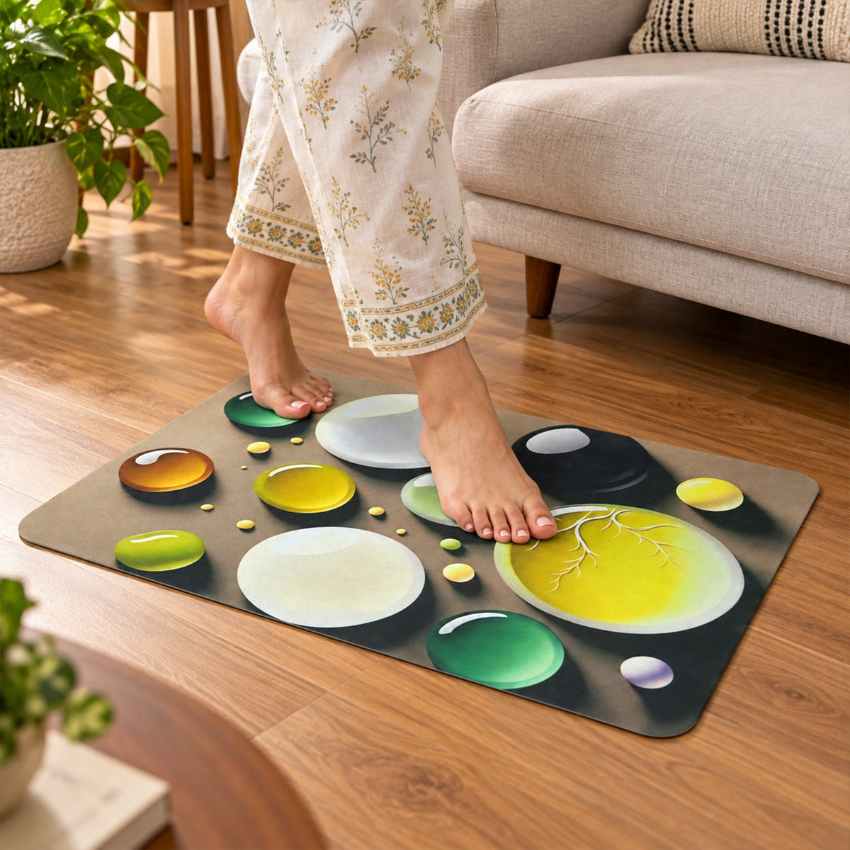 A person in patterned pants walks barefoot on a brown mat with a colorful bubble design on a wooden floor.