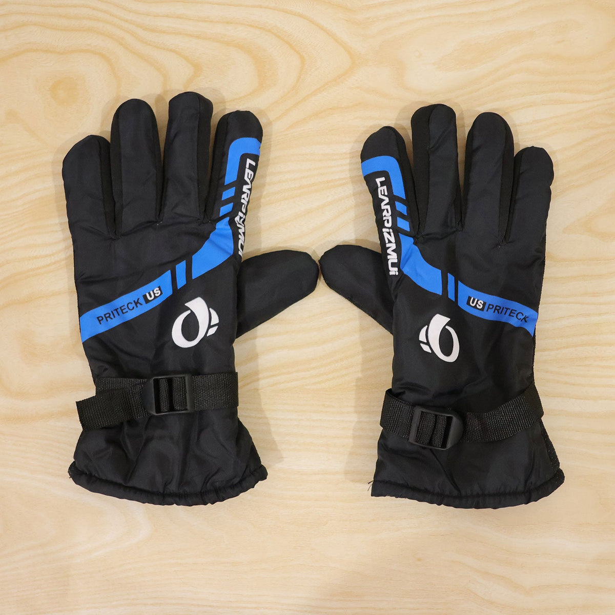A pair of black and blue winter gloves, with white logos and blue stripes, laid flat on a light wooden background.