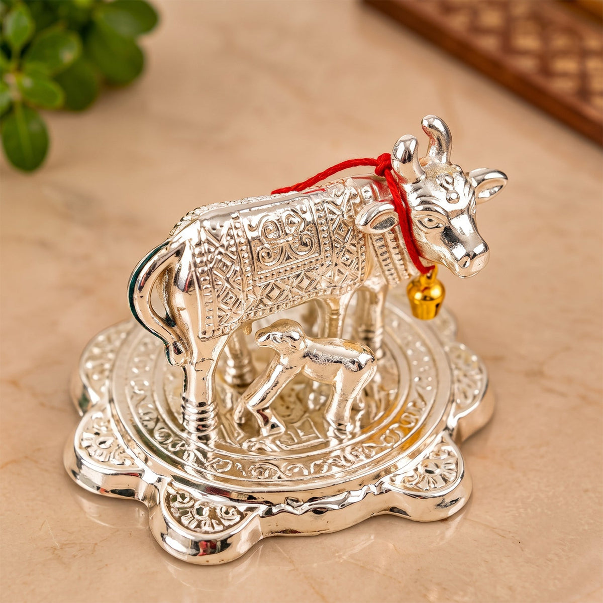 An angled shot of the silver Kamdhenu cow and calf idol on a light marble surface.