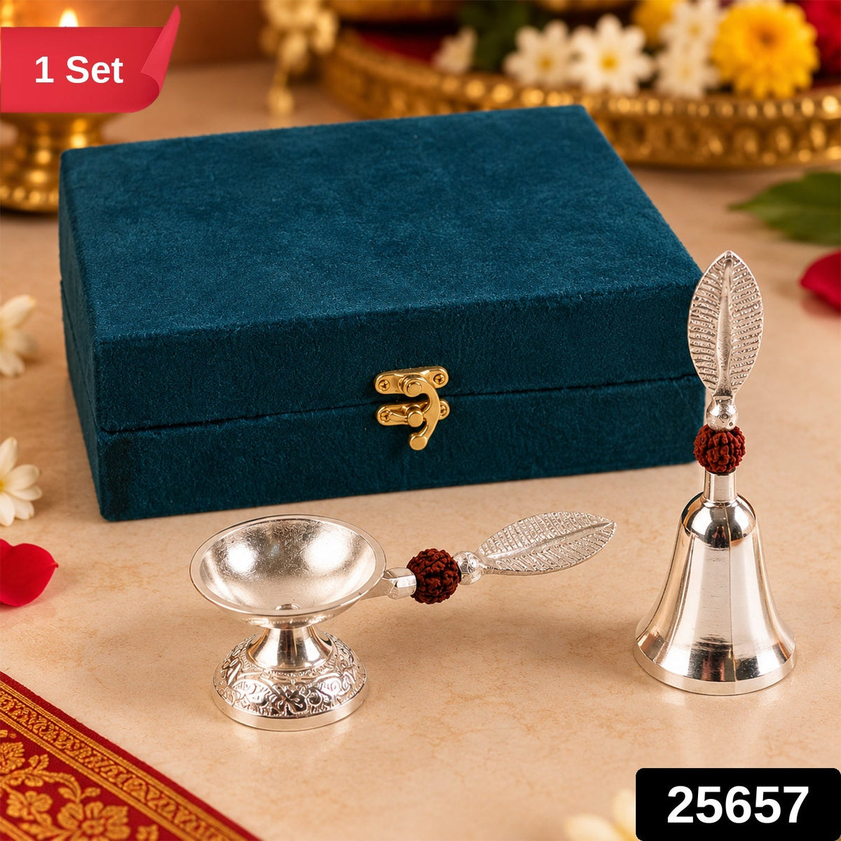 A silver finish pooja bell and diya set with leaf handles and rudraksha beads, next to a teal velvet box, with a red "1 Set"