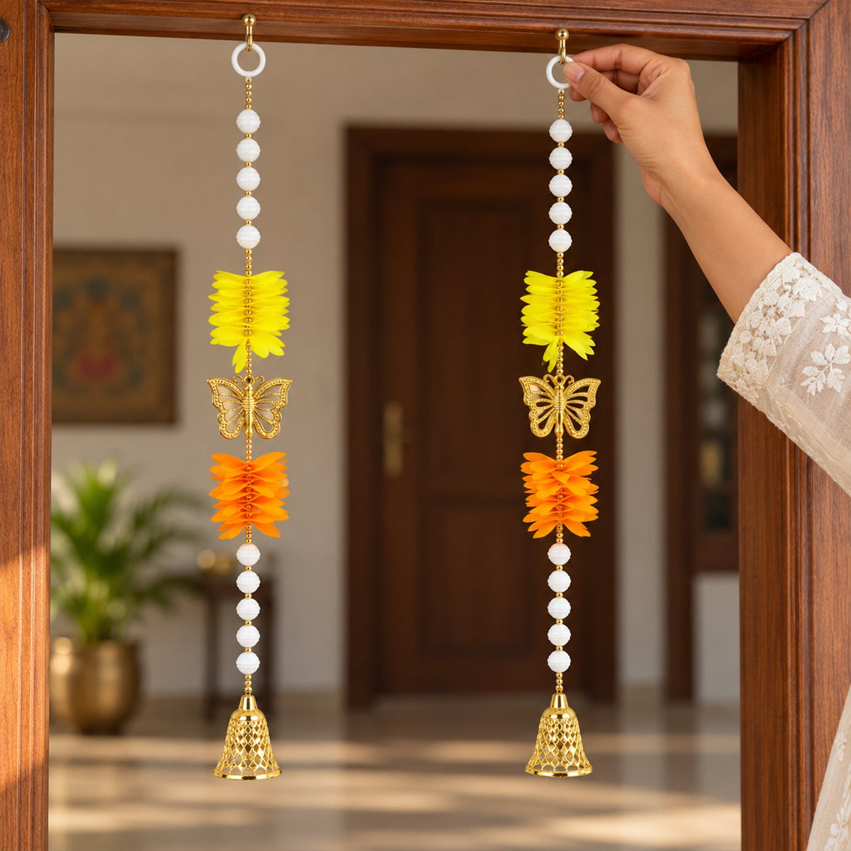 A hand adjusting one of two decorative door hangings, each with yellow and orange paper flowers, a golden butterfly, and a