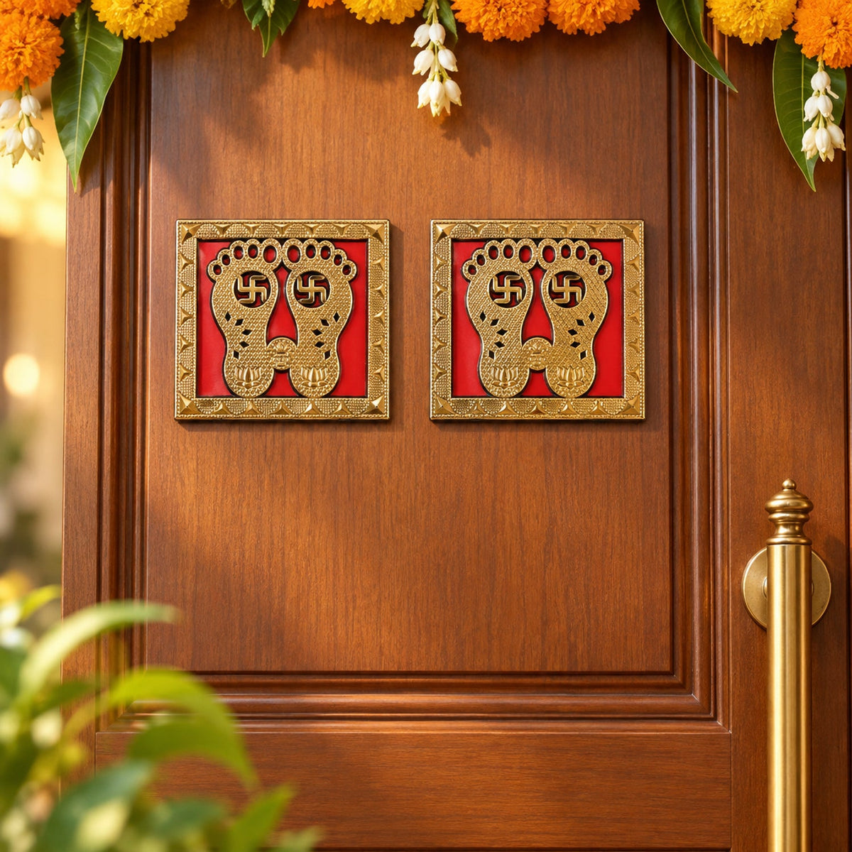 Two golden Lakshmi Charan stickers are affixed to a wooden door, decorated with orange and yellow marigold garlands and