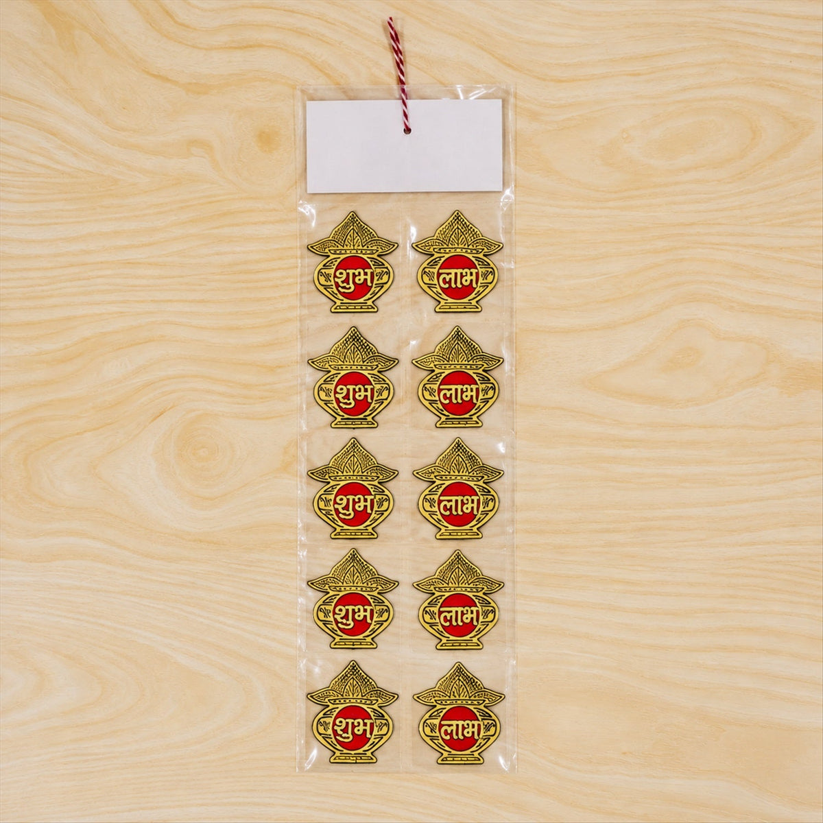 Ten golden Shubh Labh stickers are sealed in clear plastic packaging with a white label on a light wood surface.